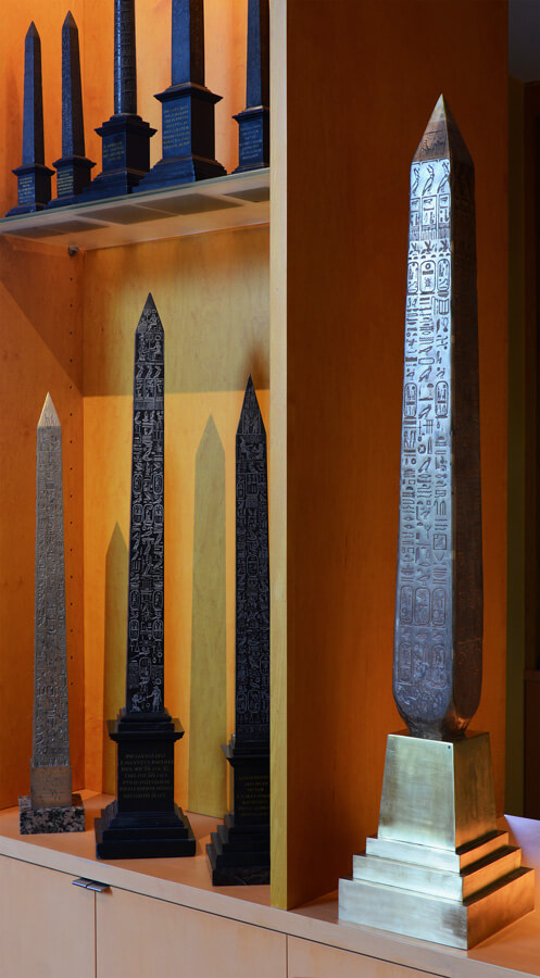 A large bronze model of London's Cleopatra's Needle stands beside a bevy of Roman obelisk models, primarily rendered in black marble.